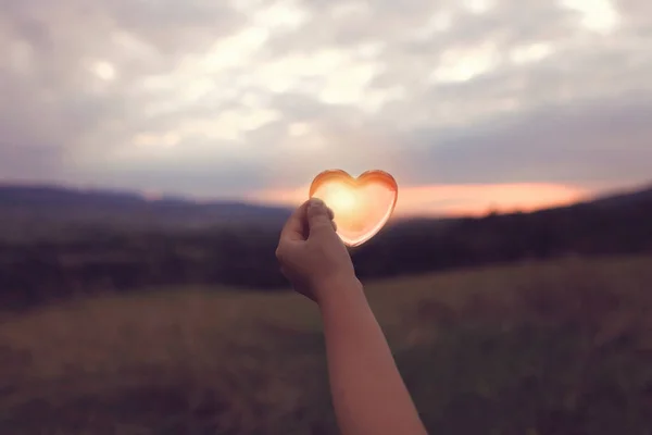 Un cuore di vetro con il sole dentro sopra cielo crepuscolare nuvoloso — Foto Stock