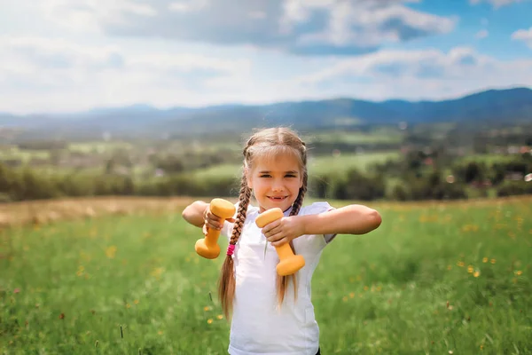 Girl doing her morning exercises with dumbbell on the top of the mountains in summer — Stock Photo, Image