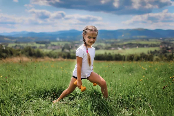 A lány, aki a reggeli gyakorlatait végzi súlyzóval a hegytetőn a nyáron. — Stock Fotó