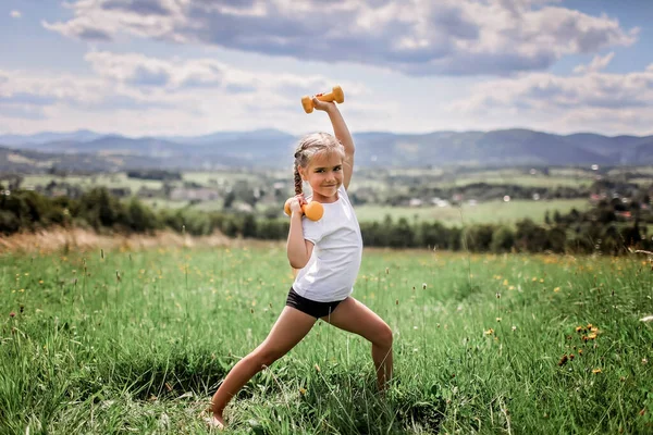 A lány, aki a reggeli gyakorlatait végzi súlyzóval a hegytetőn a nyáron. — Stock Fotó