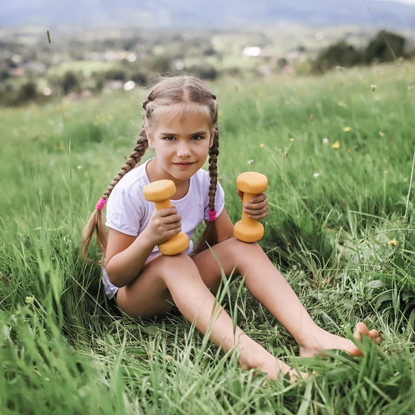 A lány, aki a reggeli gyakorlatait végzi súlyzóval a hegytetőn a nyáron. — Stock Fotó