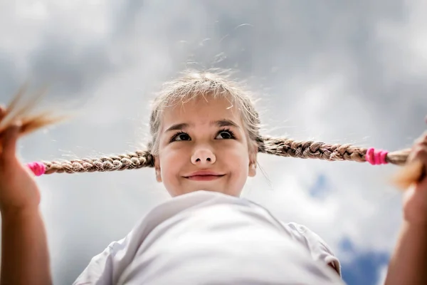 Närbild uppriktig porträtt av söt flicka med två roliga flätor tas upp på himlen från marken — Stockfoto