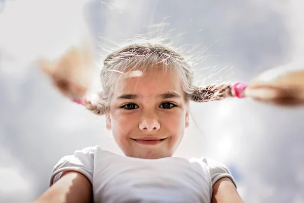 Close-up candid portrait of cute girl with two funny braids taken up at the sky from the ground — Stock Photo, Image