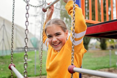 Parlak sarı kapüşonlu genç bir kızın oyun parkında oynadığı hayat tarzı fotoğrafı. Neşeli hareket ve iyimserlik duygusal esnekliği ve olumlu akıl sağlığını ifade eder.