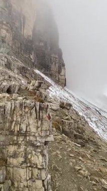 Dolomiteli yeşil ceketli kadın yürüyüşçüyle puslu kayalık dağ yolu. Yüksek kaliteli FullHD görüntüler