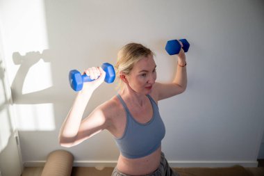 Yoga minderinde ağırlık çalışırken kadın dambılları kaldırıyor. Yüksek kalite fotoğraf