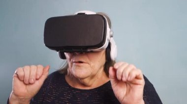 Sanal gözlüklü büyük anne evde 360 VR kaskla inanılmaz 3D videolar izliyor. Gözlüklü kadın havada bir şeye dokunmaya çalışıyor..