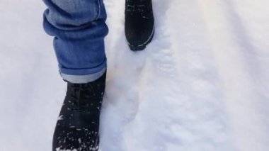 Siyah çizmeli ve mavi kotlu kadın bacakları karda yürüyor. Üst cephede. Karlı şehirde yürü.