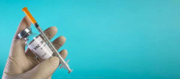 Eine Ärztin in weißen Handschuhen hält einen Coronavirus-Impfstoff und eine Spritze in der Hand. Blaues Farbbanner mit covid-19 Behandlungskonzept. — Stockfoto