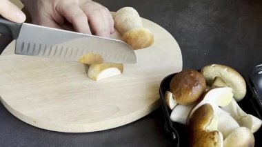 Erkeğe yaklaş ve ahşap kesim tahtasında taze mantar kes. Koyu gri mutfak masası. Yüksek kaliteli FullHD görüntüler