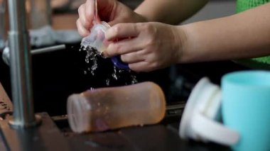 Süt için plastik bebek şişesini fırçayla temizleyen bir kadının yakın çekimi. Mutfak lavabosu. Yüksek kaliteli FullHD görüntüler