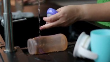 Süt için plastik bebek şişesini fırçayla temizleyen bir kadının yakın çekimi. Mutfak lavabosu. Yüksek kaliteli FullHD görüntüler