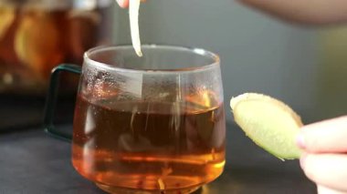 Gri mutfak masasındaki cam fincana taze zencefilli çay koyan bir kadın. Sağlık için antioksidan bitkisel içecek. Yüksek kaliteli FullHD görüntüler