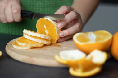 Kadın eli kapalı, tahta kesme tahtasıyla taze portakal meyvesi kesiyor. 