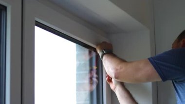 Bir evin mutfak penceresine beyaz panjur takan beyaz bir adamın, günışığının modern plisses tonları. Yüksek kaliteli FullHD görüntüler