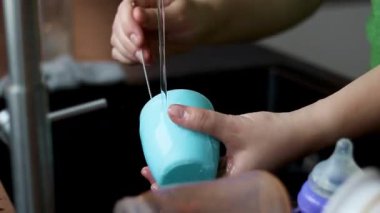 Mutfak lavabosunda küçük bir çocuk için dökülmemiş bardağı temizleyen bir kadına yakın çekim. Yüksek kaliteli FullHD görüntüler