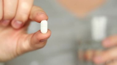 Beyaz bir hap ve su dolu bir bardak tutan bir dişinin fotoğrafını çek, ev kavramında ağrı kesici. Yüksek kaliteli FullHD görüntüler