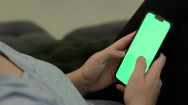 Kanepede oturan ve yeşil ekranlı akıllı telefon kullanan bir kadının fotoğrafını çek. Yüksek kaliteli FullHD görüntüler