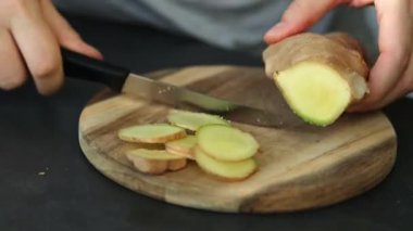 Dişi ellerin, tahta kesme tahtasındaki bıçakla taze zencefili kesmesi. Yüksek kaliteli FullHD görüntüler