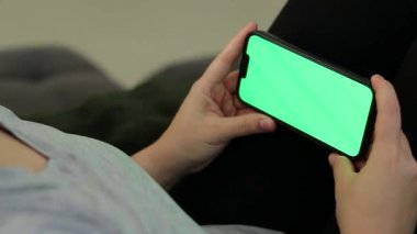 Kanepede oturan ve yeşil ekranlı akıllı telefon kullanan bir kadının fotoğrafını çek. Yüksek kaliteli FullHD görüntüler