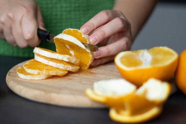 Kadın eli kapalı, tahta kesme tahtasıyla taze portakal meyvesi kesiyor.