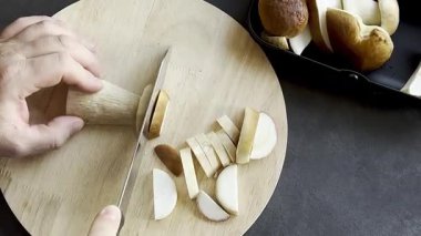 Erkeğe yaklaş ve ahşap kesim tahtasında taze mantar kes. Koyu gri mutfak masası. Yüksek kaliteli FullHD görüntüler