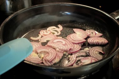 Kavrulmuş taze kırmızı soğanları siyah tavada yakın plan, modern indüksiyon sobası.