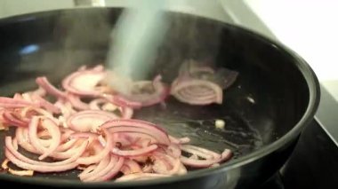 Siyah tavada kırmızı soğan, yağlı mavi silikon spatula, modern indüksiyon soba. Yüksek kaliteli FullHD görüntüler