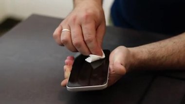 Koyu gri masadaki bir mendille telefonun ekranını silip temizleyen bir erkeğin ellerini kapatın. Yüksek kaliteli FullHD görüntüler