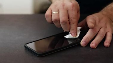 Koyu gri masadaki bir mendille telefonun ekranını silip temizleyen bir erkeğin ellerini kapatın. Yüksek kaliteli FullHD görüntüler