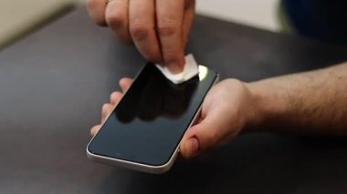 Koyu gri masadaki bir mendille telefonun ekranını silip temizleyen bir erkeğin ellerini kapatın. Yüksek kaliteli FullHD görüntüler