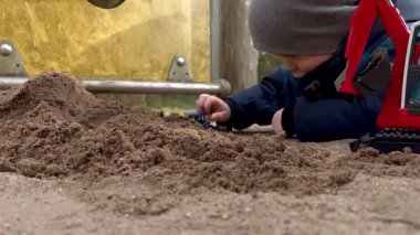 Kum havuzunda oyuncaklarla oynayan, baharda şapka ve ceket giyen küçük bir çocuğun yakın çekimi.