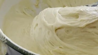Kalın hamurlar beyaz bir kaseye karıştırılıyor, kremsi dokuları sergiliyor ve pişirme amaçlı malzemelerin kademeli olarak harmanlanması