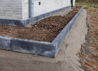 Yeni inşa edilmiş beton kenarlar modern tuğla bir evin yanında çamurla dolu bir bahçe yatağı, gelişmekte olan peyzaj çalışmalarını gösteriyor.