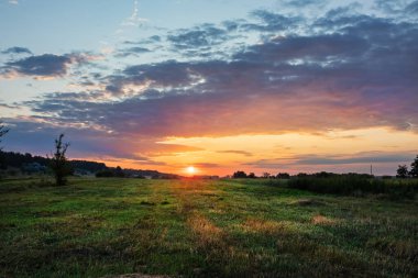 Gökyüzünde çimenler ve bulutlar olan bir çayırın üzerinde güzel bir gün doğumu. Avrupa ormanlarının bozkırlarının doğası