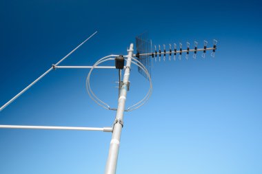 simple antenna mast with antennas to receive digital TV and radio signals, DVB-T, DVB-T2 and FM (horizontal polarization) including delayed lightning rod. The background is pure blue sky.