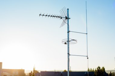simple antenna mast with antennas to receive digital TV and radio signals, DVB-T, DVB-T2 and FM (horizontal polarization) including delayed lightning rod. In the background the peaks of roofs.