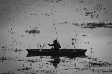 Göldeki küçük bir teknede bir balıkçının silueti.