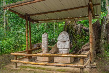 San Agustin arkeoloji parkındaki yemyeşil bitki örtüsüyle çevrili iki antik taş heykel, Kolombiya 'daki UNESCO Dünya Mirası sahası..