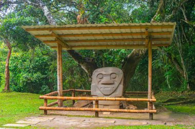 Kolombiya 'nın San Agustin Arkeoloji Parkı' ndaki bambu bir yapı tarafından korunan Kolombiya öncesi taş heykel. Etrafı yemyeşil bitkilerle çevrili..