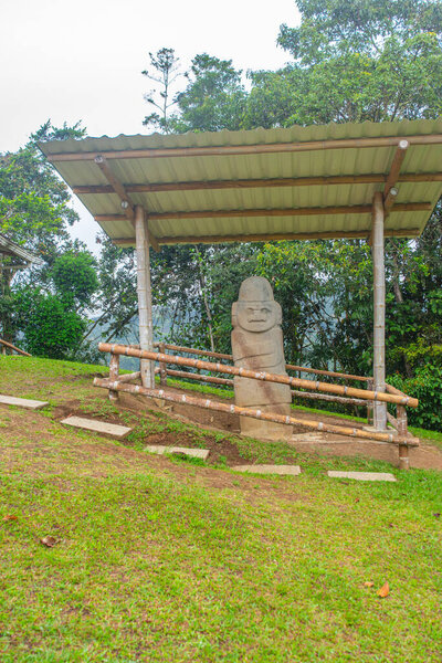 A stone statue depicting pre-Columbian art in San Agustin, Huila, Colombia, surrounded by lush greenery and UNESCO World Heritage site.