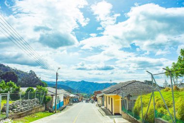 Purace, Cauca 'da bir yol manzarası. Renkli evler ve açık mavi gökyüzünün altında yuvarlanan tepeler..