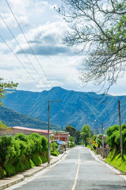 Purace, Popayan, Cauca, Kolombiya 'da yemyeşil ve bulutlu bir gökyüzünün altındaki dağlarla çevrili bir yol manzarası..