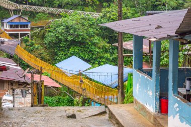 Yeşillikler arasında evleri birbirine bağlayan sarı asma köprünün canlı görüntüsü.