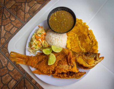 Kızarmış balık, pirinç, muz, mercimek çorbası ve limon dilimleriyle servis edilen taze salata içeren canlı bir Kolombiya deniz ürünleri tabağı..