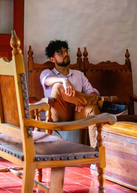 Düşünceli genç bir adam ahşap mobilyalarla dolu bir odada oturuyor, sıcak bir atmosferde düşüncelerini yansıtıyor..