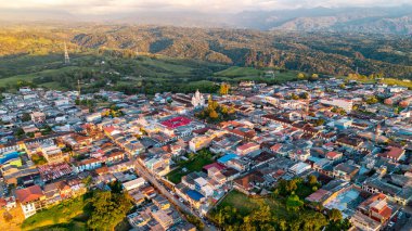 Filandia 'daki renkli çatıları gösteren büyüleyici bir manzara, altın bir günbatımı gökyüzünün altında canlı yeşil tepelerle çevrili..