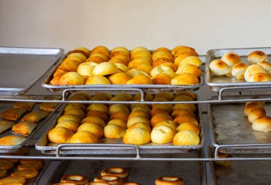 Altın ekmek ruloları, metal tepsilerde düzenli bir şekilde, çeşitli şekil ve boyutlarda, sıcak bir ortamda sergileniyor..