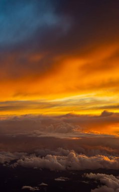 Canlı bir günbatımı ılık turuncu ve sarı renkleri kabarık bulutlar arasında bırakır ve alacakaranlık gökyüzünün çarpıcı bir hava manzarasını yaratır..