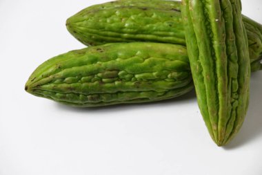 Endonezya yemeklerinde popüler bir tropikal sebze olan yeşil acı sukabaklarının kapağı temiz beyaz bir yüzey üzerinde taze ve izole bir şekilde sergilenmektedir..